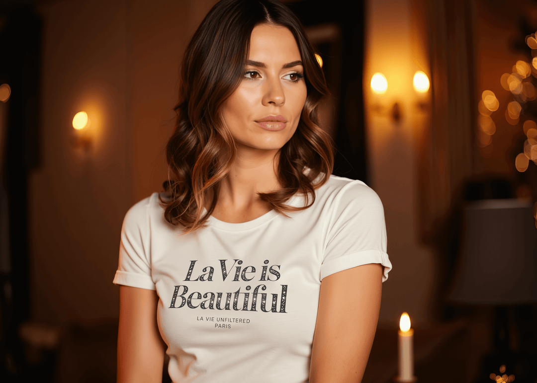 Woman wearing a white La Vie Is Beautiful tee in a softly lit room decorated with warm holiday lights