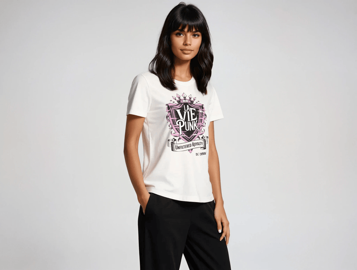 Model wearing the Punk Majesty Allure jersey tee in white featuring bold La Vie Punk crest graphic with pink crown and banner reading Unfiltered Royalty, styled with black pants against a light gray background.
