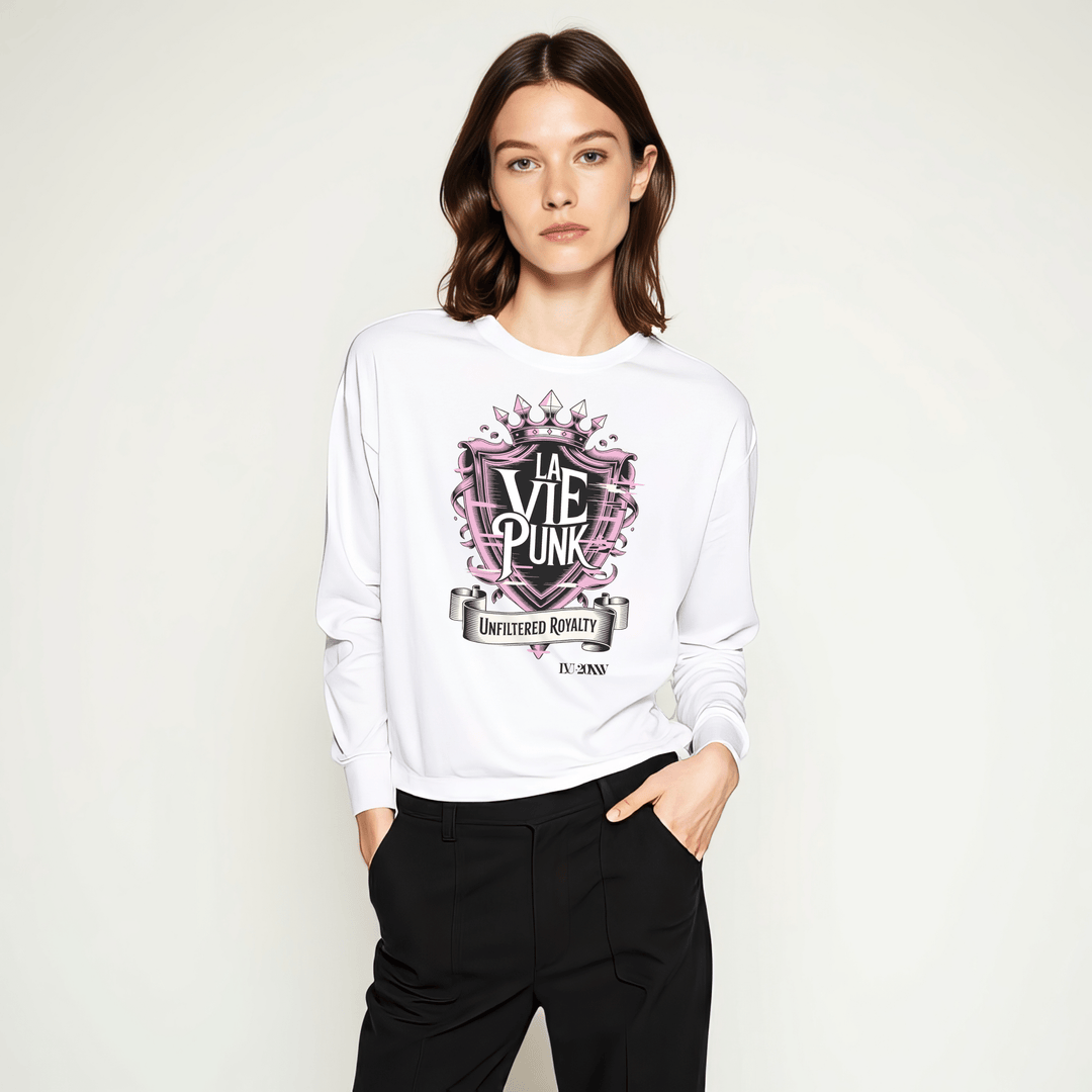 Model wearing white long-sleeve t-shirt with pink and black crown-inspired ‘LA VIE PUNK’ graphic and ‘Unfiltered Royalty’ banner, styled with black trousers in a studio setting.