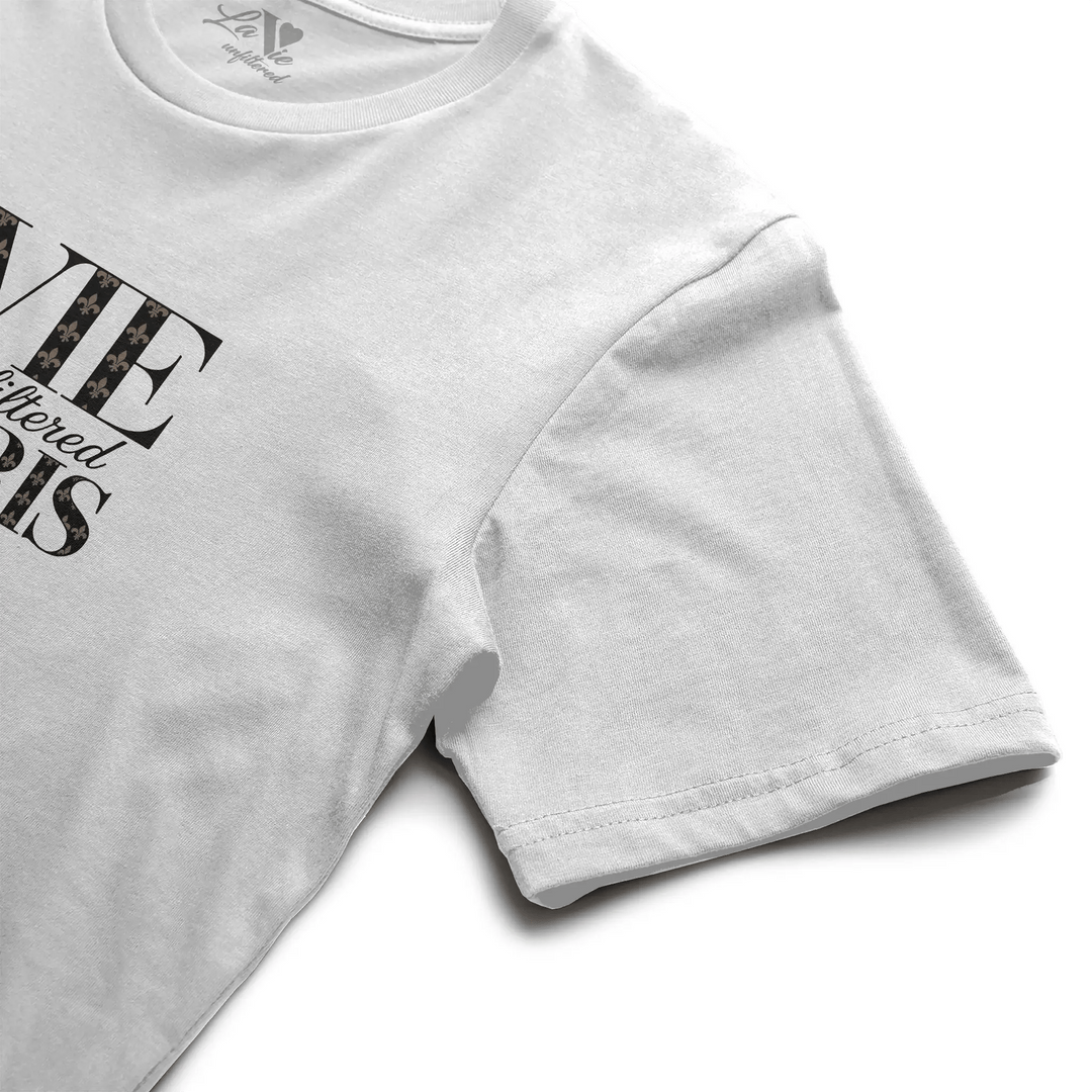 Close-up angled view of neckline and chest design of the white boxy fit tee, featuring 'La Vie Unfiltered Paris' with noir monogram details.