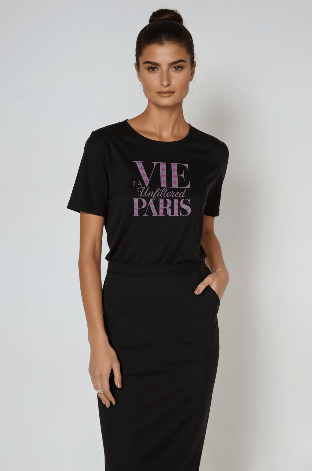 Model wearing black boxy-fit short sleeve tee with purple 'La Vie Unfiltered Paris' graphic, styled with a high-waisted black skirt in a studio setting.