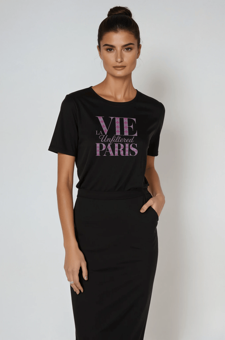 Model wearing black boxy-fit short sleeve tee with purple 'La Vie Unfiltered Paris' graphic, styled with a high-waisted black skirt in a studio setting.