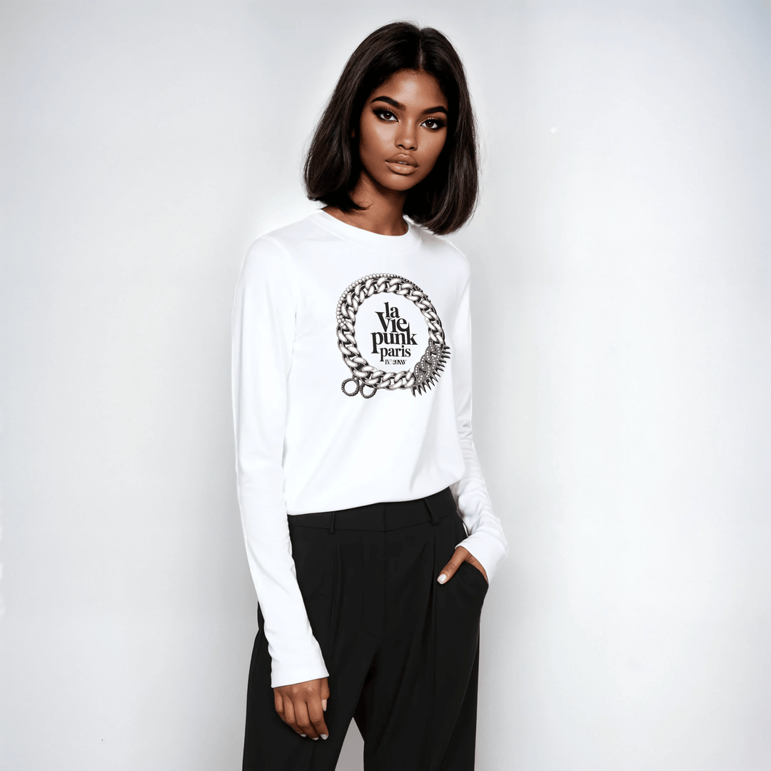 Woman wearing white long-sleeve tee with La Vie Punk Paris emblem graphic, styled with black tailored pants.