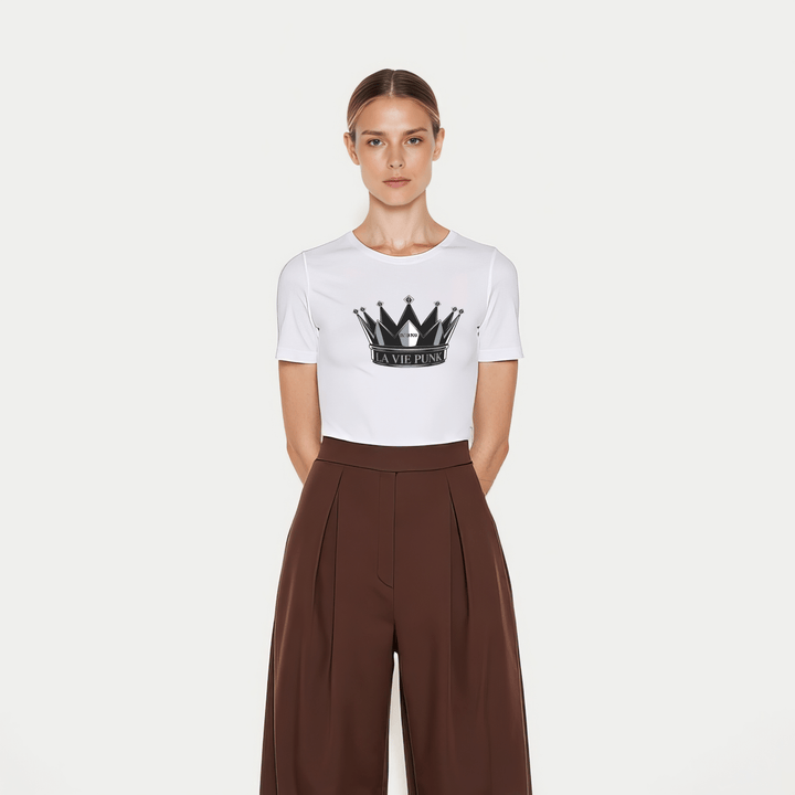 Model wearing the Throne Punk Allure jersey tee in white with a bold black crown graphic and 'La Vie Punk' lettering, styled with high-waisted brown wide-leg trousers, photographed on a plain white background.