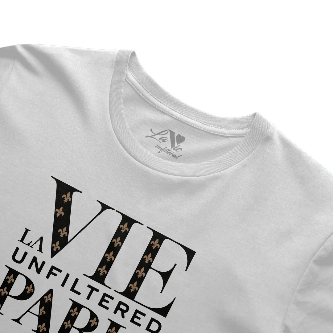 Close-up angled view of white boxy fit tee with 'La Vie Unfiltered Paris' noir monogram print and visible La Vie unfiltered neck tag.